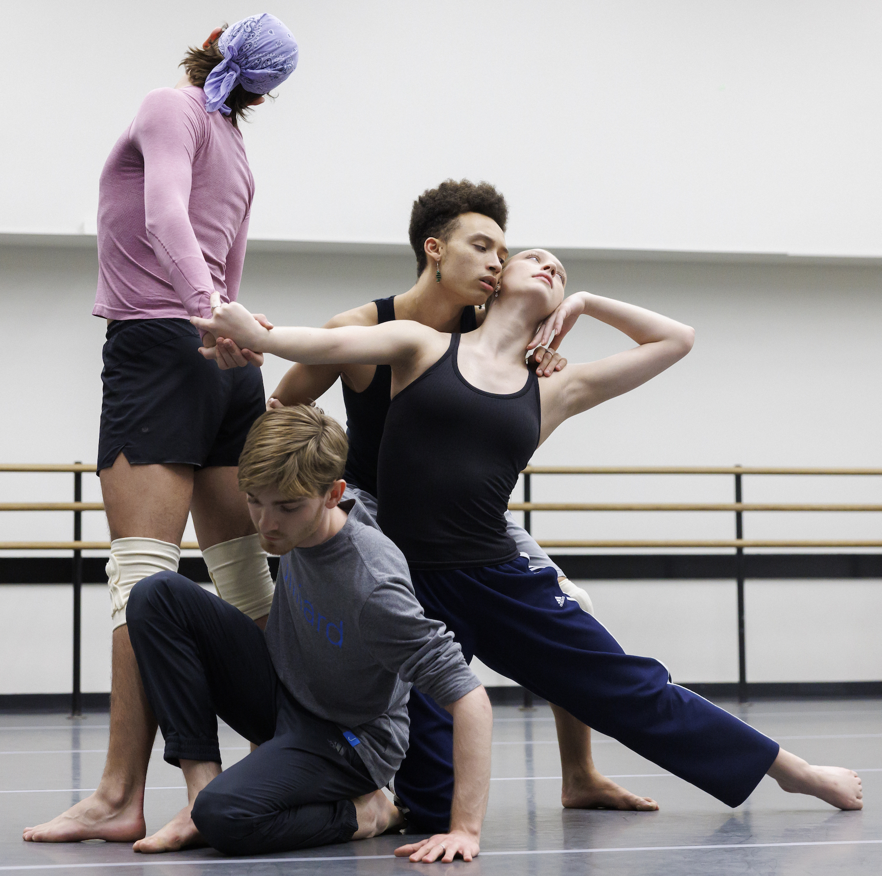 Four dancers in a group pose in the midst of rehearsal in a dance studio