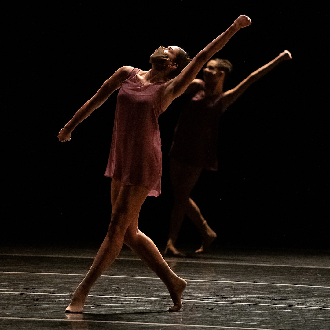 Two dancers in the midst of performance make a triumphant pose with their left arms in the air