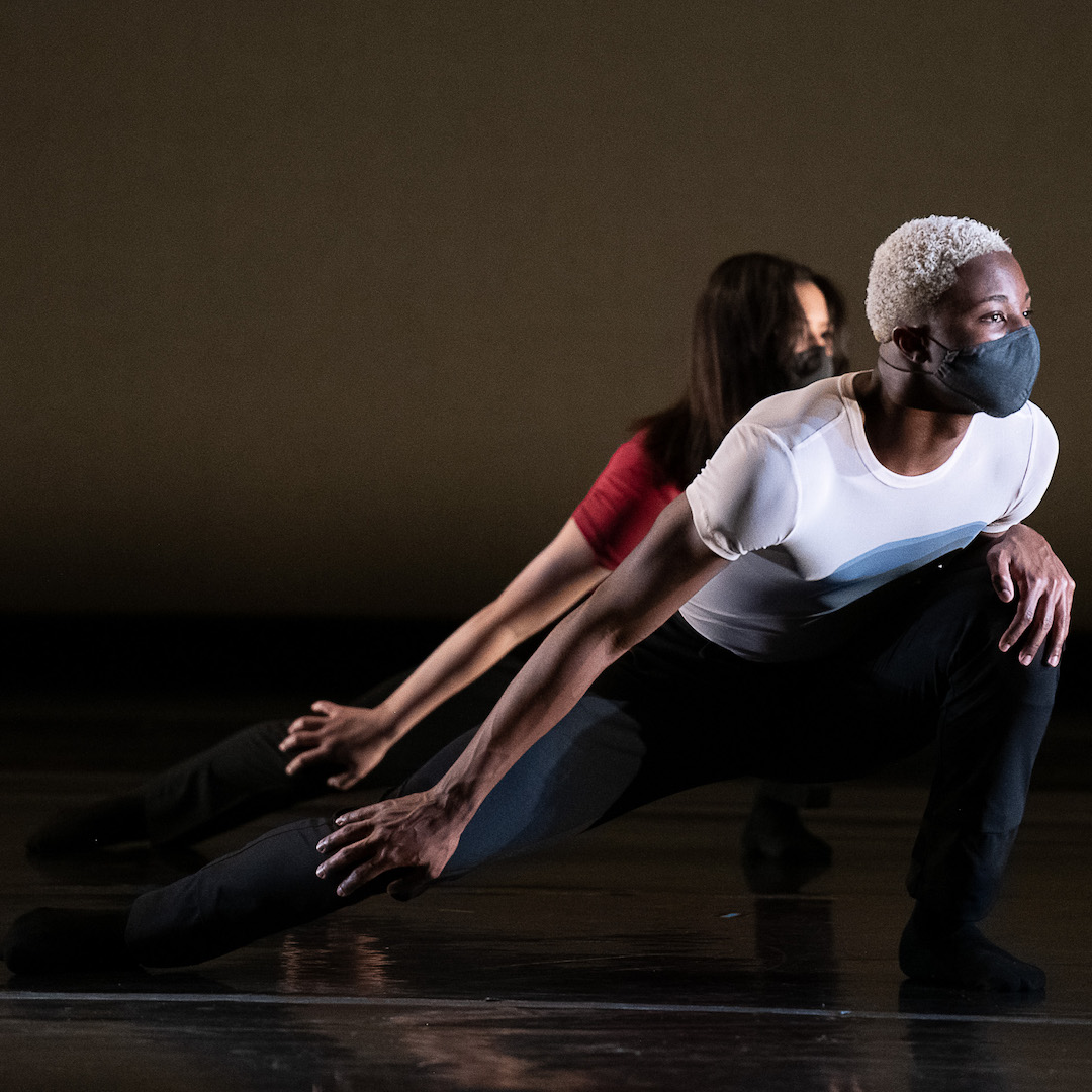 Two dancers in the midst of performance come forward into a deep lunge, each resting their hand on their knee