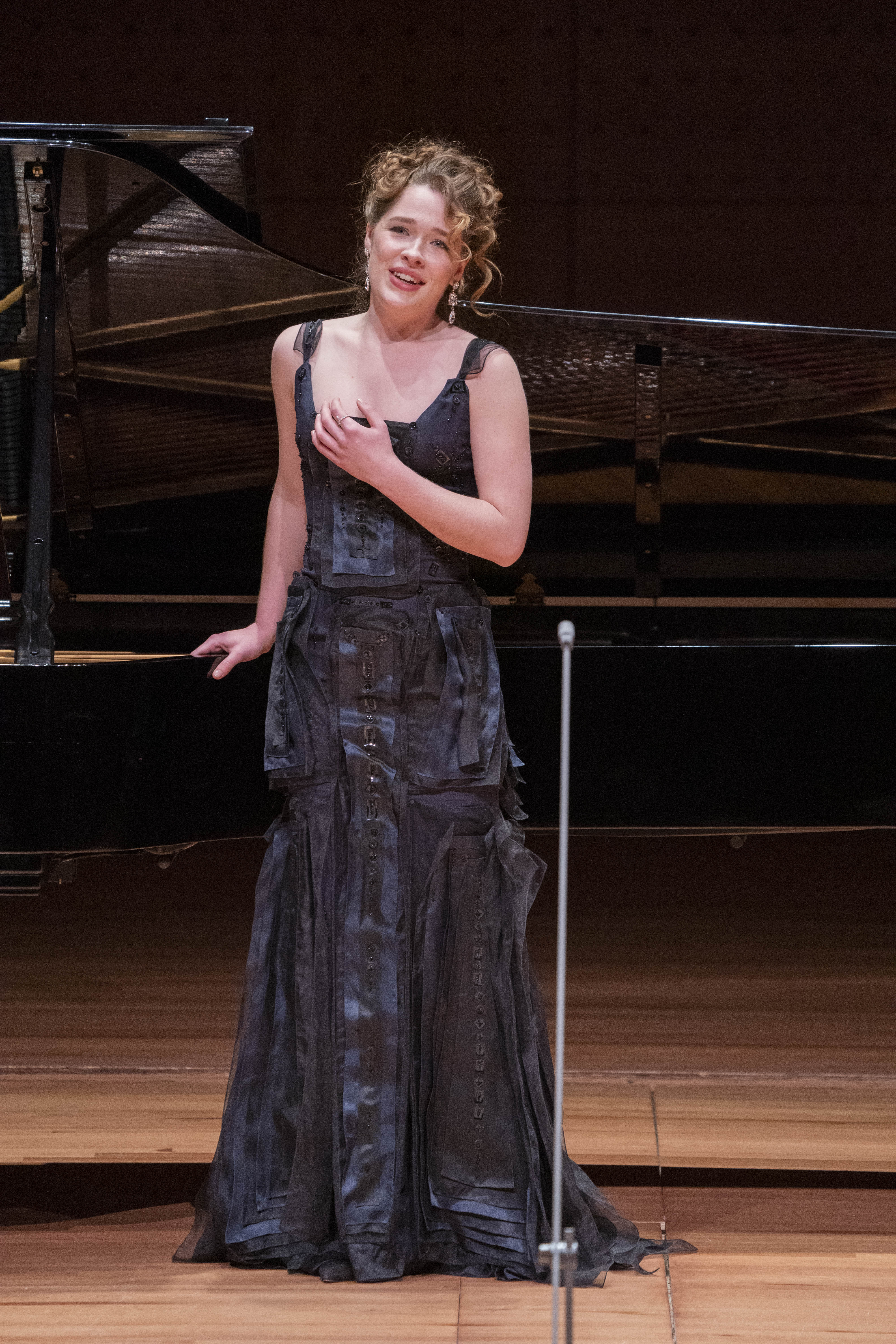 Xenia Puskarz Thomas is singing on stage in front of the piano in this performance photo