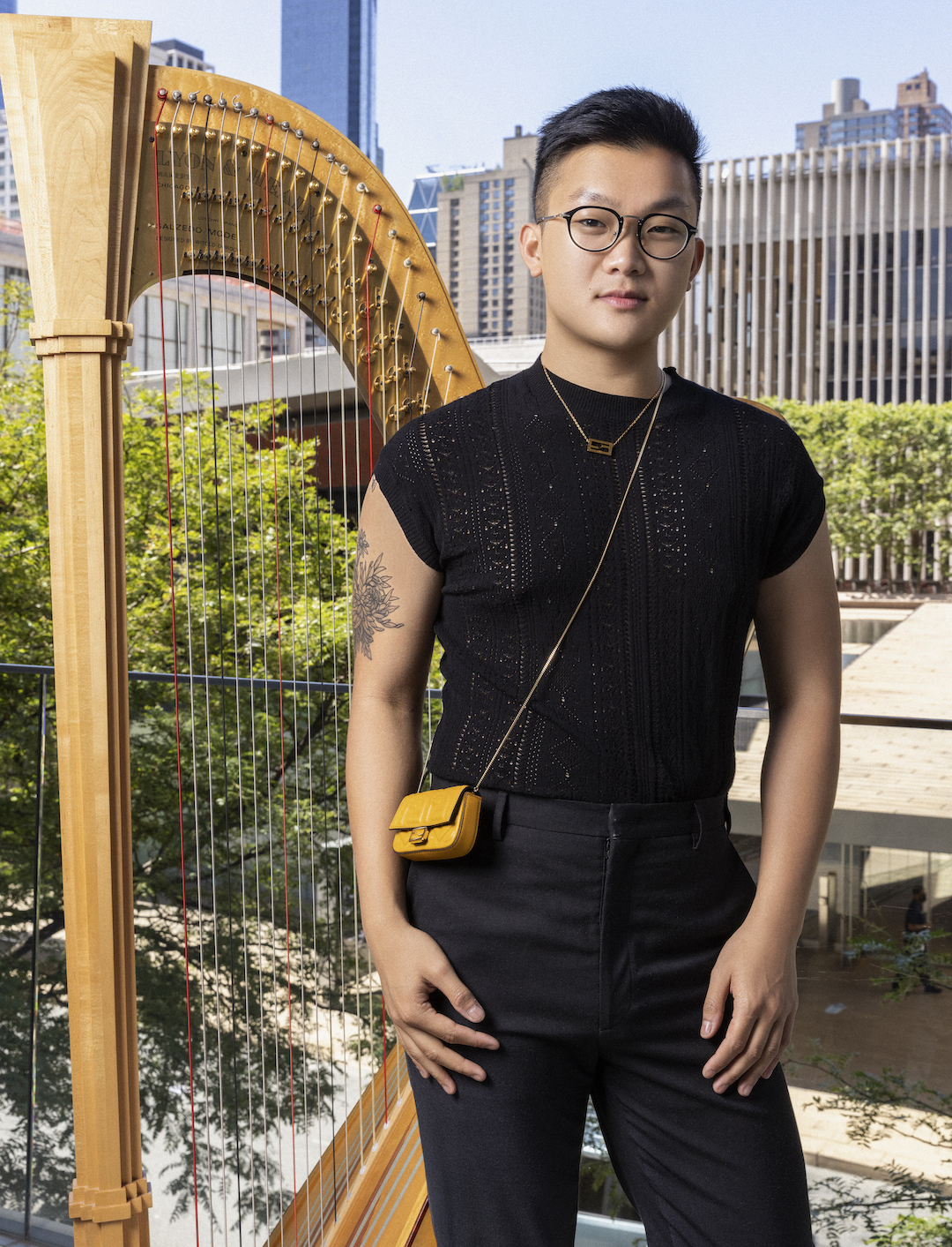 A harp player wearing Fendi attire poses with his harp outside
