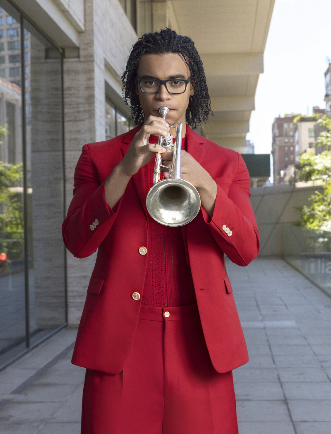 A trumpet player wearing a fire engine red Bermuda shorts suit posing outside with his horn