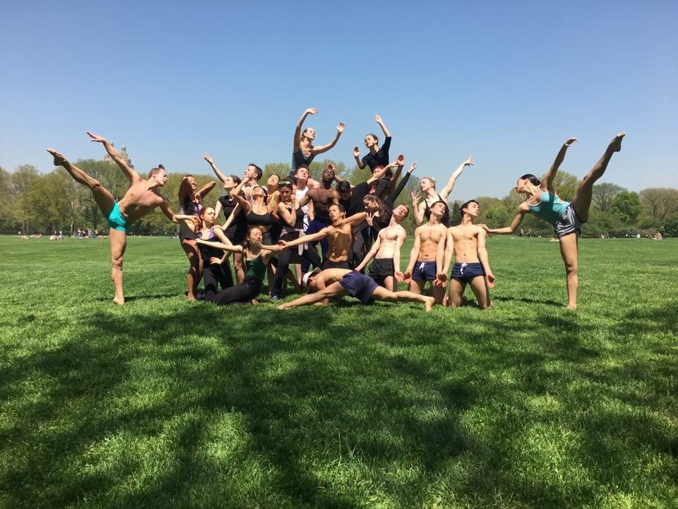 A group of dancers pose outside on grass