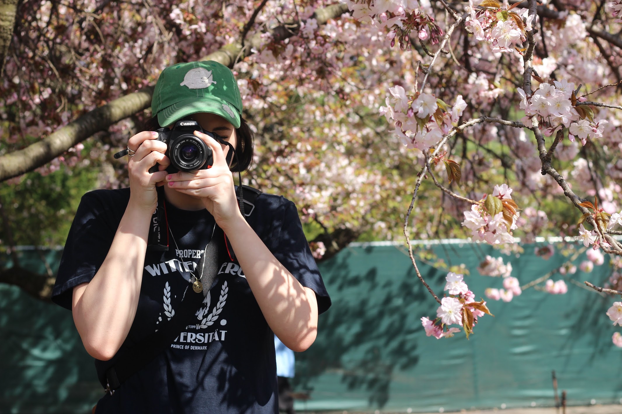 Mei poses with a camera in front of a cherry blossom tree