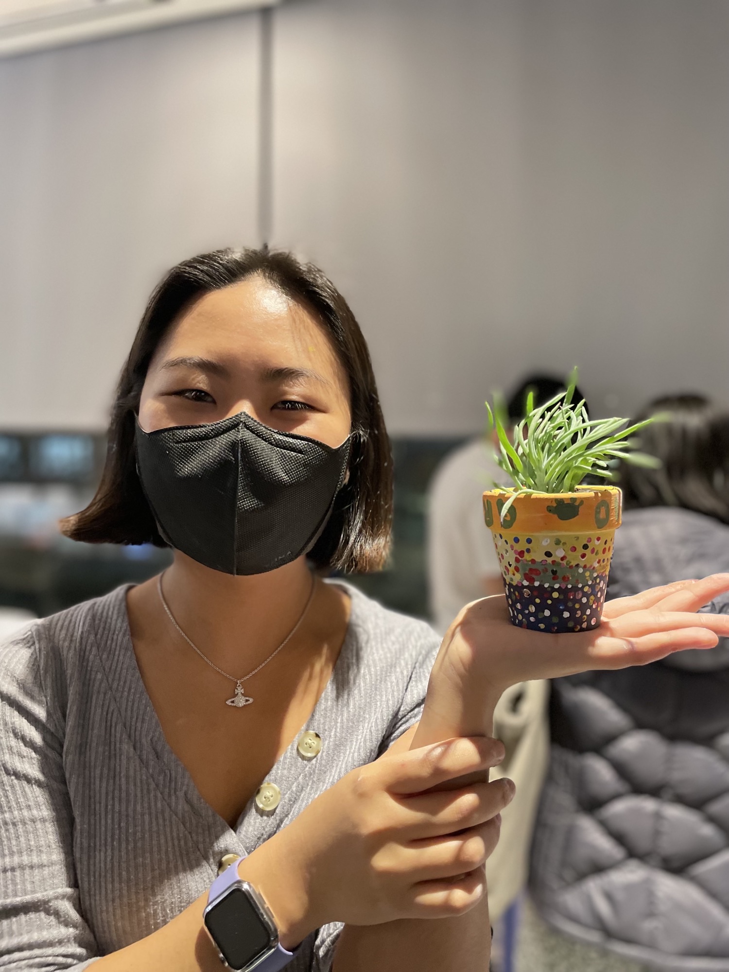 A student wearing a mask poses with a potted plant