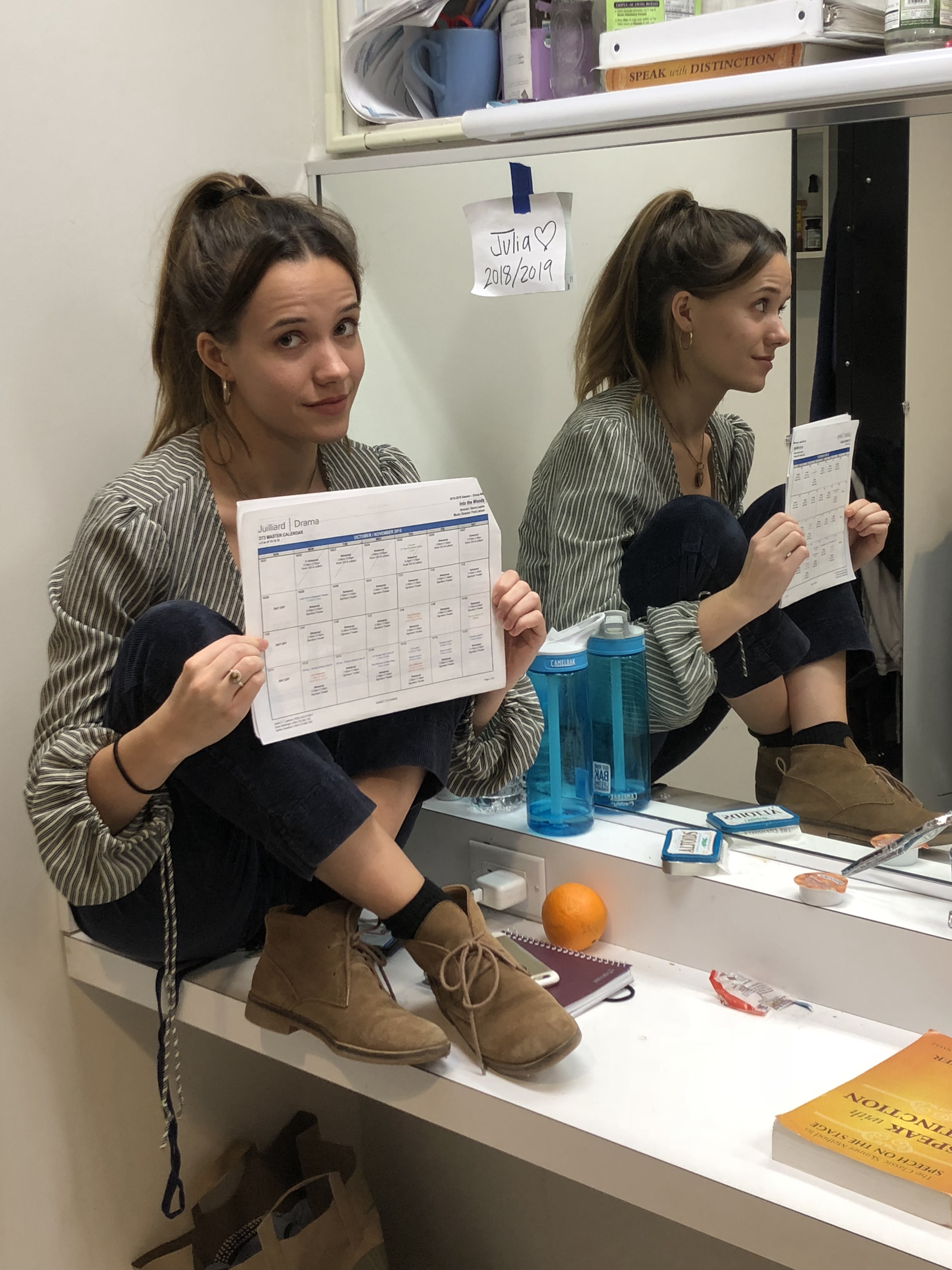 Julia seated on a dressing room table and holding her schedule