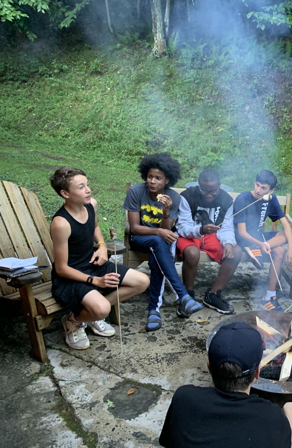 A group of teenagers sitting around a campfire in an outdoor setting