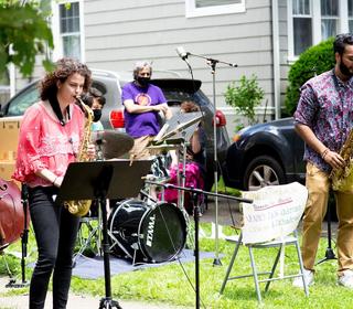 A jazz combo performing outdoors, on the lawn of a suburban home