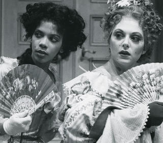 Two ladies in period costume fan themselves, their eyes askance in an expression of intrigue
