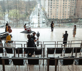 Six musicians, dressed in Fendi clothing, playing as part of a jazz combo with two film crew members in the photo to communicate a behind-the-scenes perspective