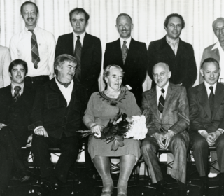 An archival, black and white photo of Mme. Renée Longy is seated center for a portrait style photo with students