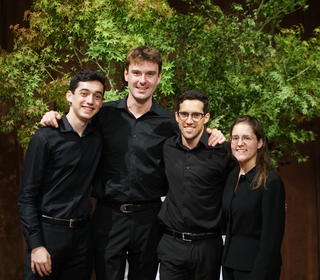 Spencer Rubin and his friends pose for a group photo in front of a shrub. They are dressed in performance black.