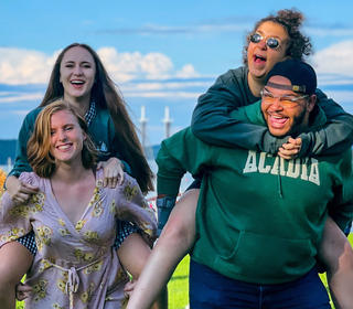 Four people having a fun time and smiling by the water on a sunny, blue-skied day