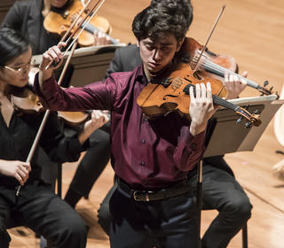 Sean Juhl playing viola on stage with a group of musicians behind him