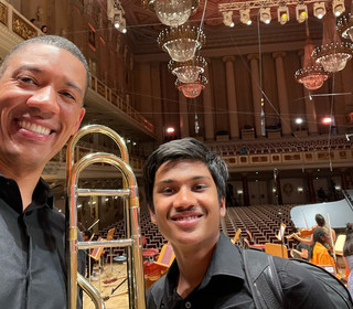 Weston Sprott and Agastya Batchu pose for a selfie in a concert hall. They are holding their instruments and smiling.