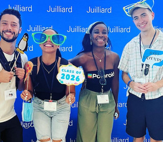 Four smiling students stand in front of a blue step-and-repeat that has Juilliard's logo on it