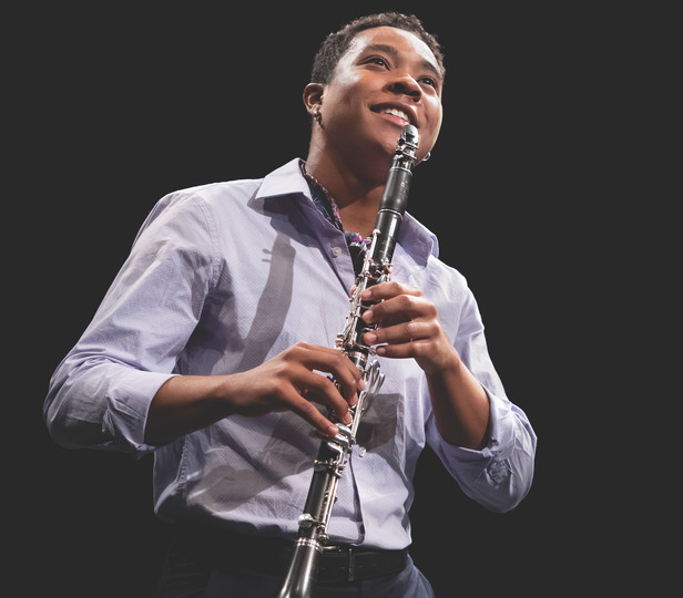A smiling student is on stage holding a clarinet and poised to begin playing