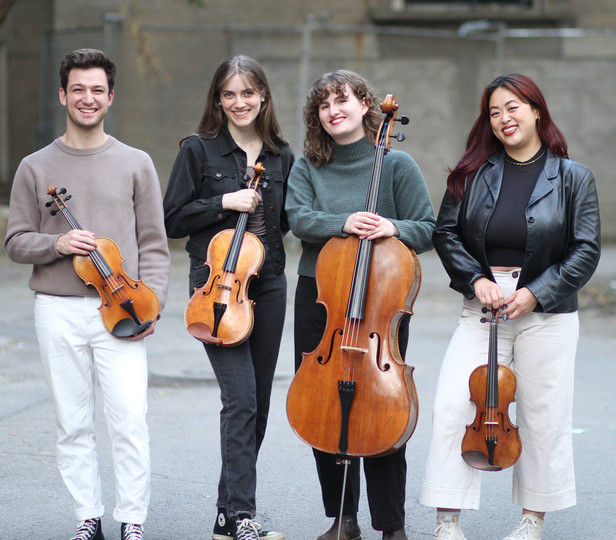 string quartet members standing outside and posing for photo behind a building