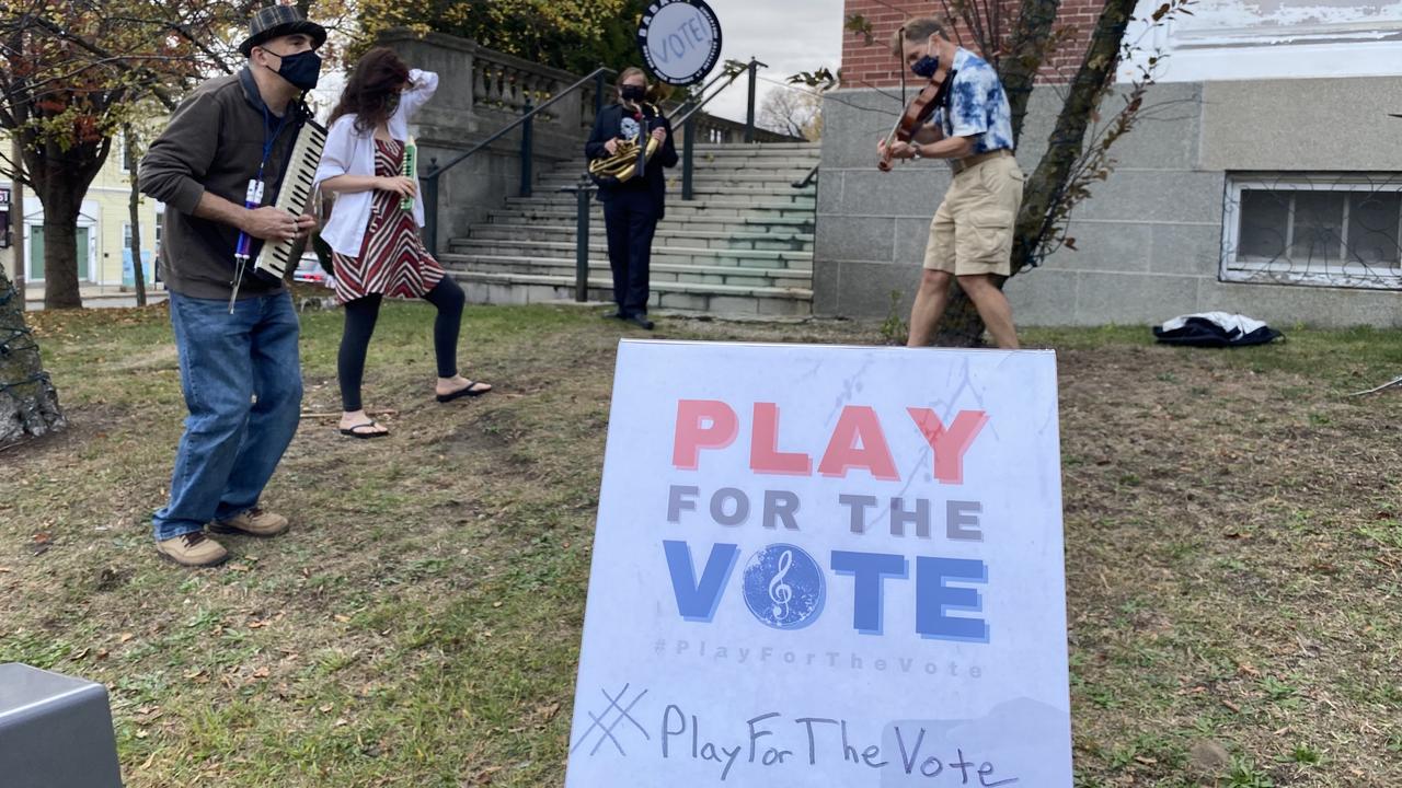 A group of musicians perform outside with a sign that says Play for the Vote
