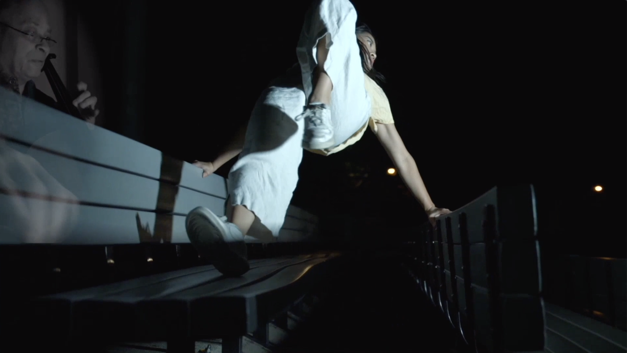 At night—a dancer, dressed in white, extends backward and a faint image of a musician, ghostlike, has been overlaid to the side, conveying that this is a dance and music collaboration