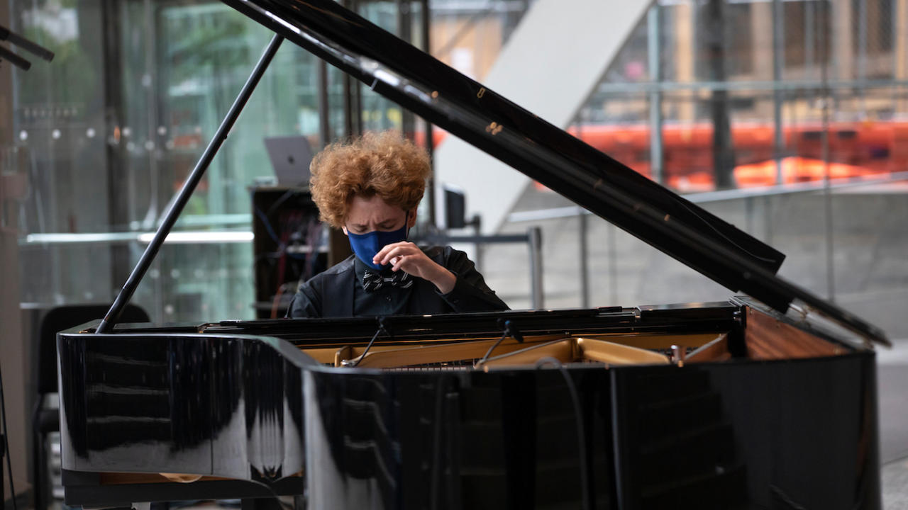 A student, masked, playing the piano in the lobby of Alice Tully Hall