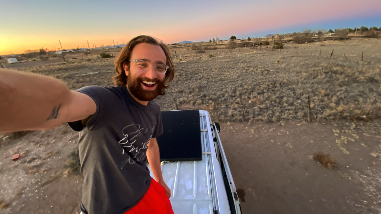 Theo Hoffman standing on the roof of his van, taking a selfie, and a beautiful sky fills the background