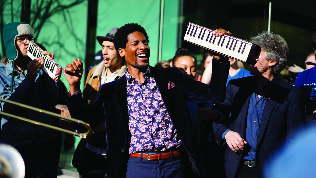 Jon Batiste outdoors with a group of students and holding his melodica