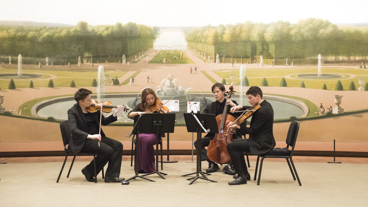 A string quartet performing in front of a large mural depicting a classical garden scene. The players are deeply engaged in their music. The setting, highlighted by the grand mural of a baroque garden with neatly trimmed hedges and statues, adds a formal and historic ambiance to their performance. The musicians, dressed in concert attire, enhance the elegant and artistic atmosphere of the scene.