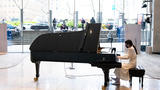 A pianist is playing in the lobby of Alice Tully Hall and through the windows onlookers are visible