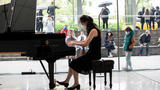 Katherine Wang is playing piano in the lobby of Alice Tully Hall and onlookers are visible through the glass