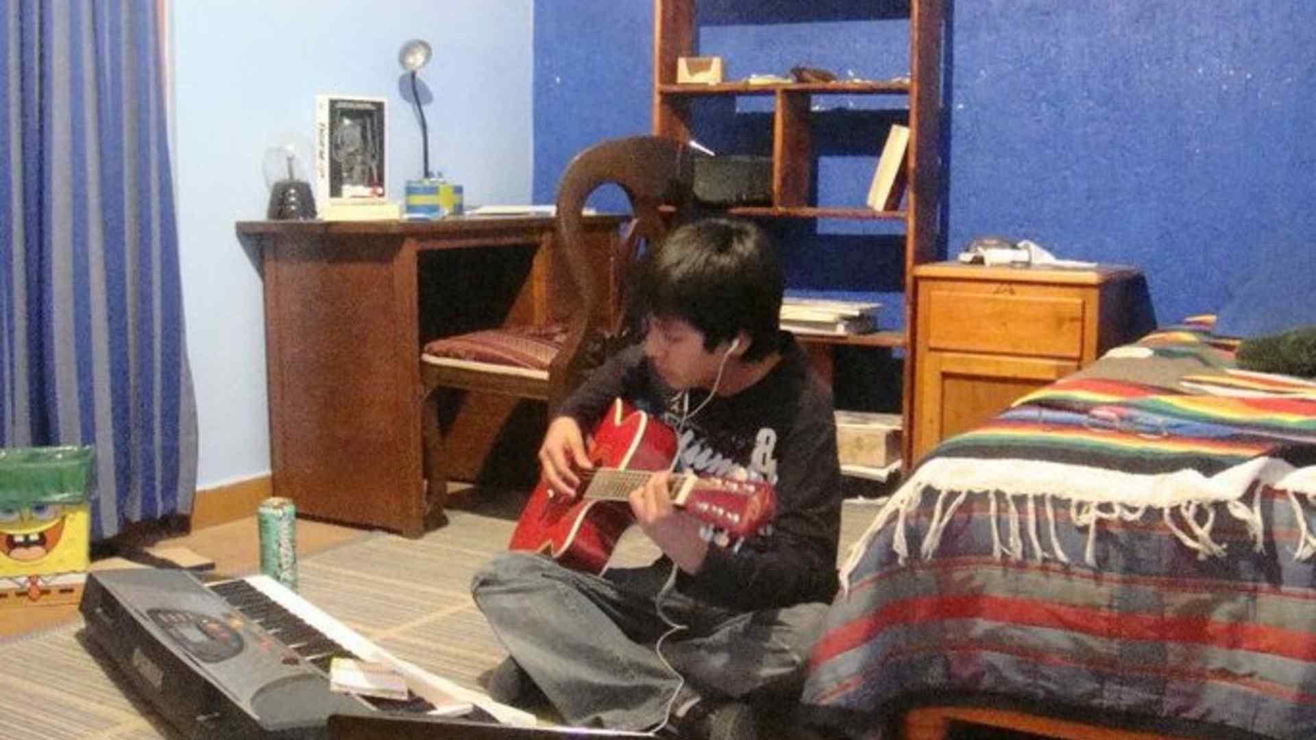 Young Horacio playing guitar on the floor of his room