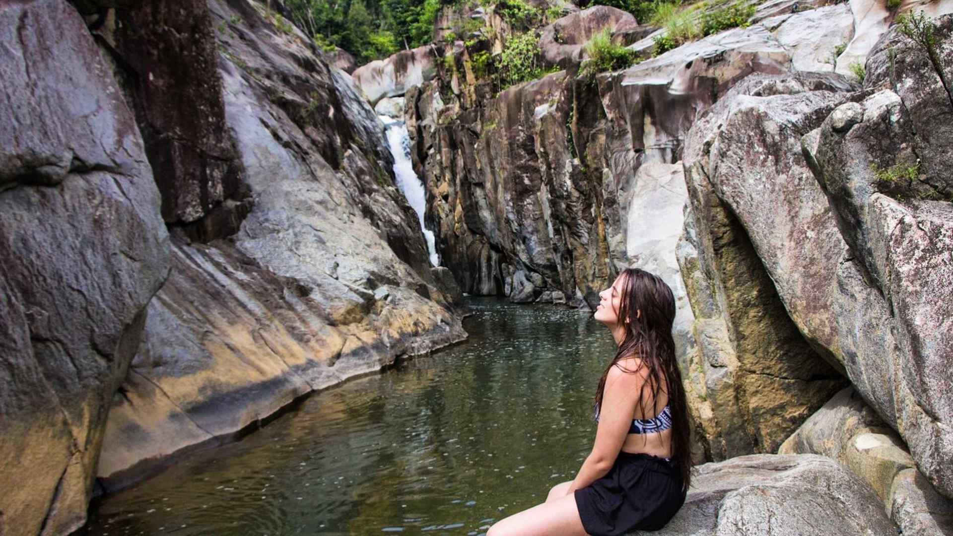Gabriela sits on a rocky cliff by a waterfall