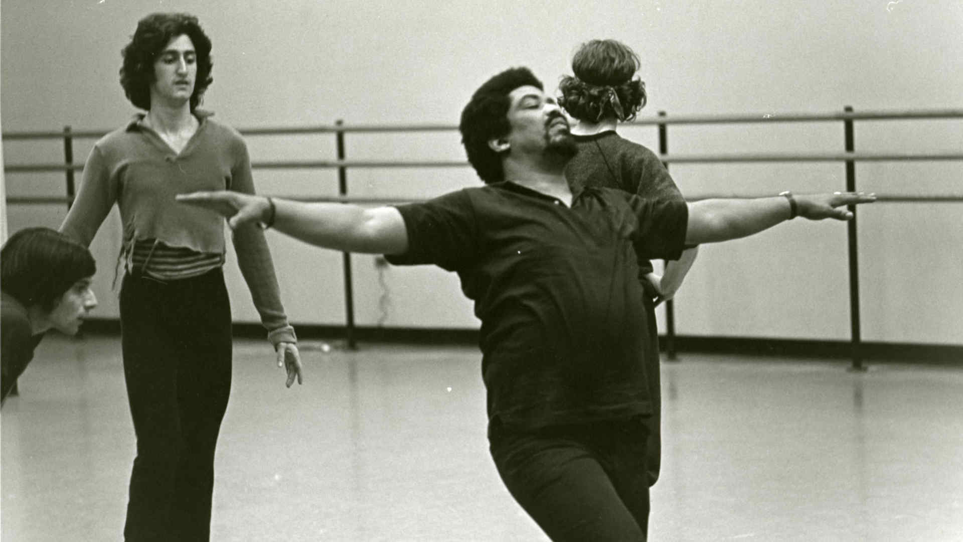 Archival (black and white) photo of a dance rehearsal in a studio, ballet barre visible in the background, and the photo features Gregory Mitchell, a Juilliard alum