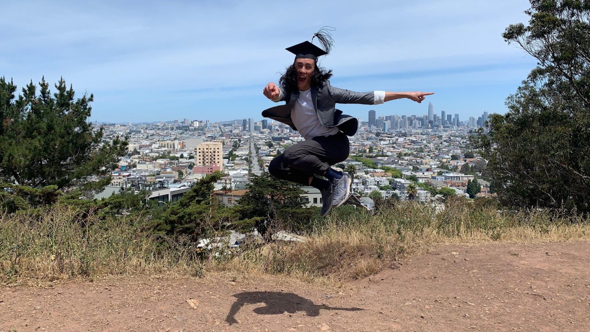 Noah Wang, in cap and gown, leaping into the air