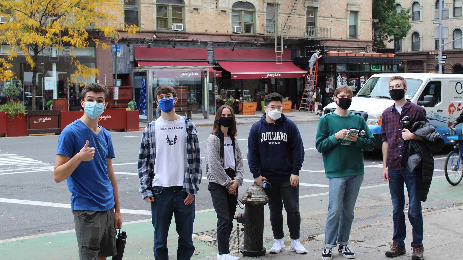 Six first-year students, each wearing a face mask, pose casually near a fire hydrant on a New York City street