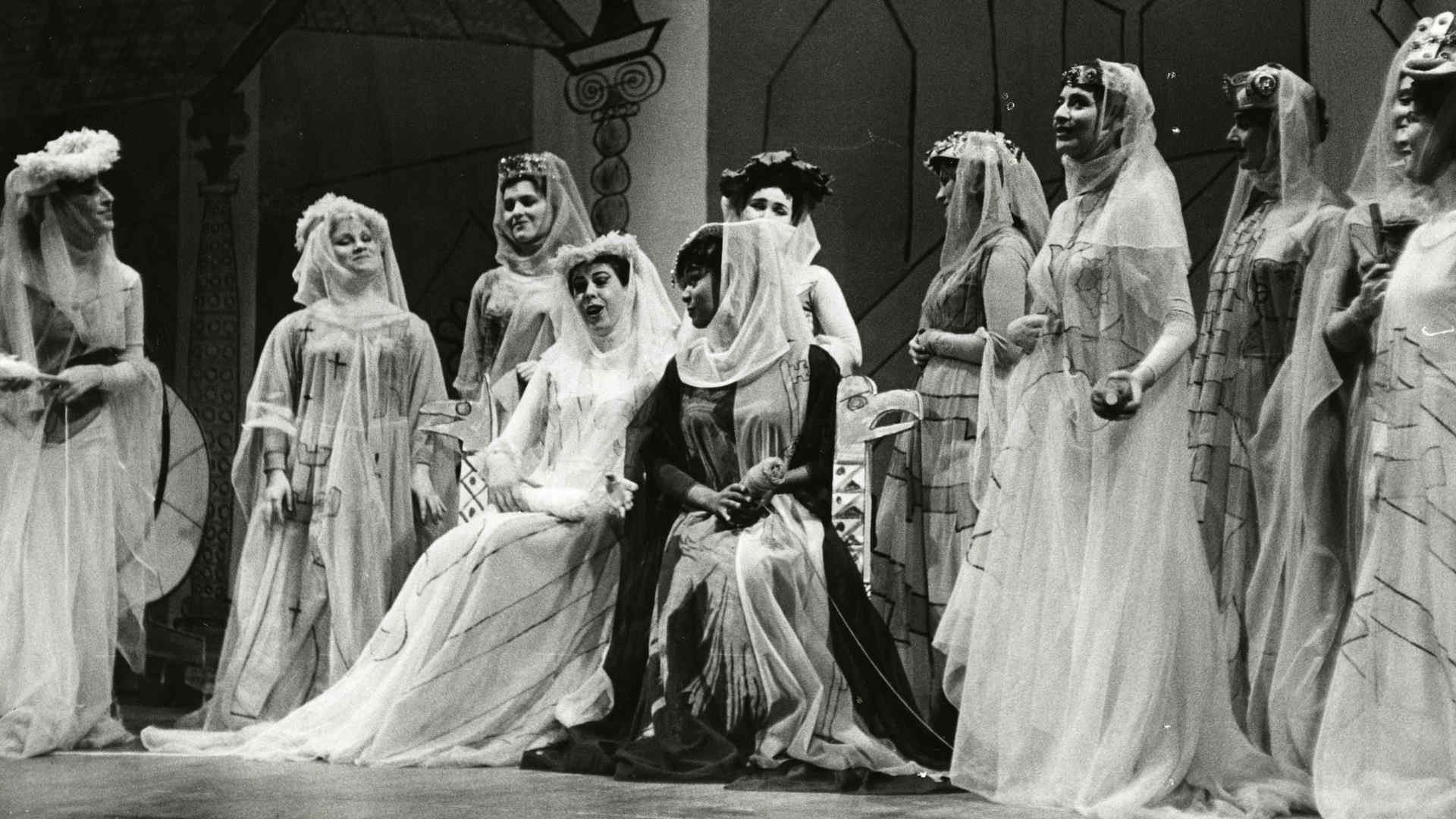 About 10 women in white, flowing dresses on stage in this archival photo from the opera production