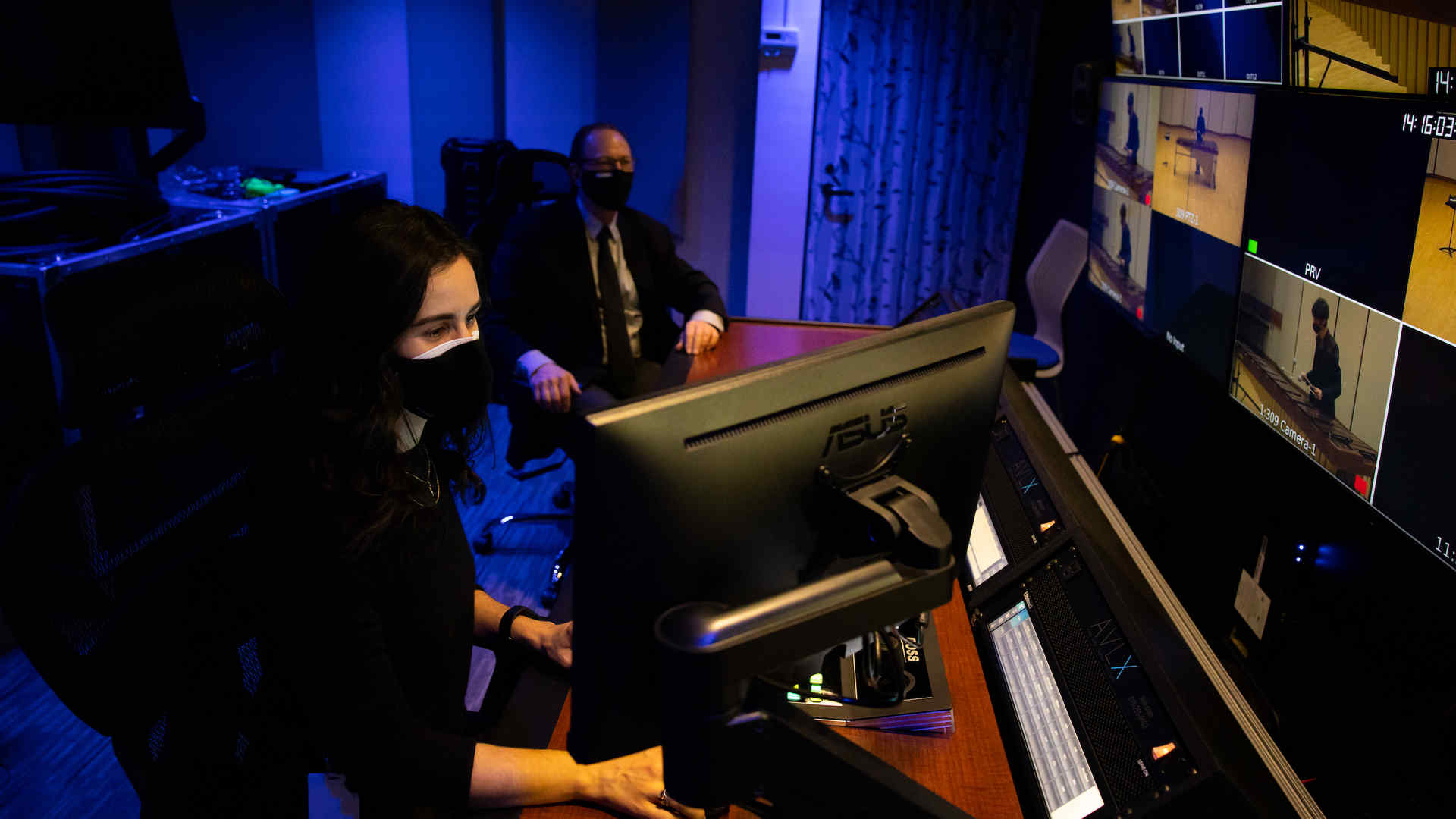 Elizabeth Svokos and Kevin Boutote sitting in a control room at Juilliard. The dimly lit room is illuminated by numerous television monitors and Elizabeth and Kevin are concentrated on a particular screen