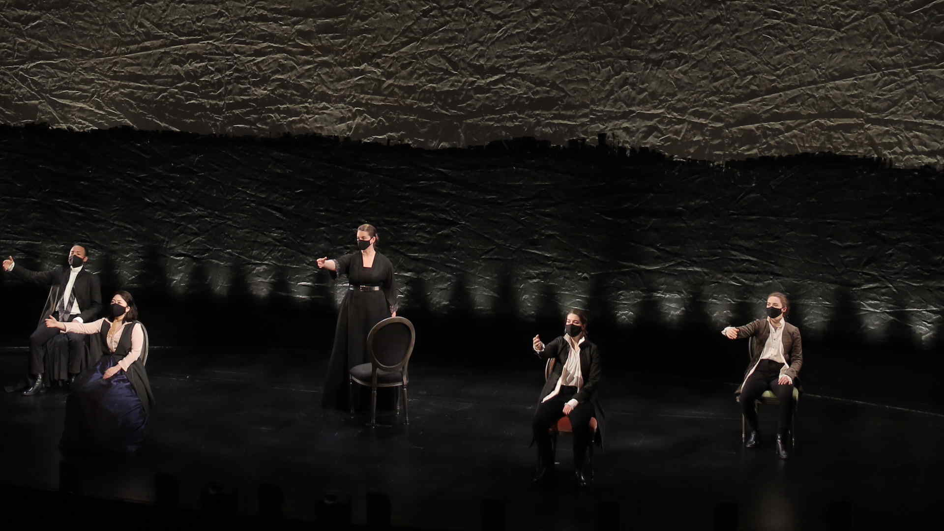 Performance photo of singers, masked and costumed, socially distanced in this posed scene with their arms extended all in a similar direction