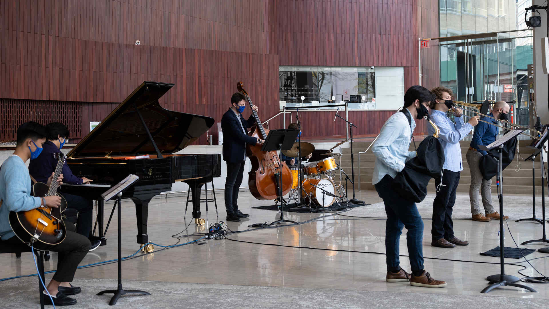 A combo of seven jazz musicians is playing in the lobby at Alice Tully Hall and visible on the floor are wires for recording and sound amplification equipment—indicating that this is a live performance