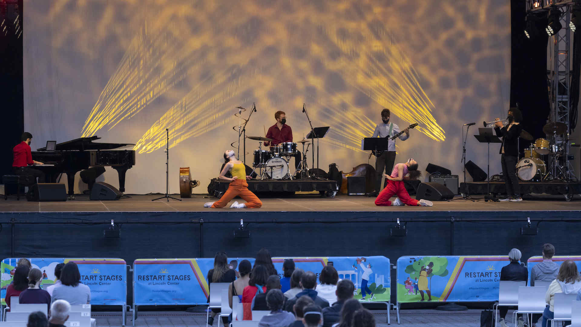 Musicians and dancers on an outdoor stage. The audience is also visible.
