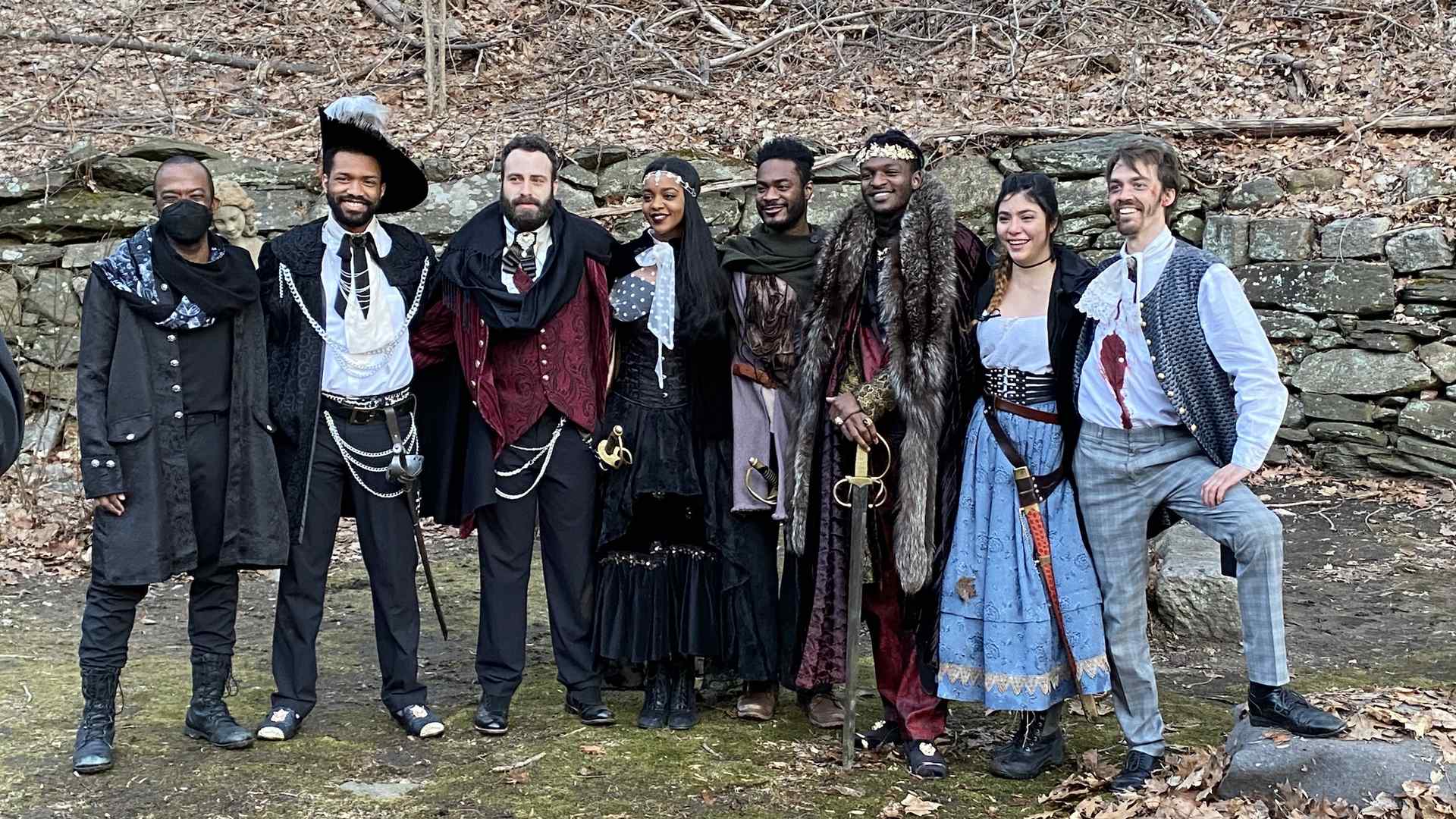 Shaun Patrick Tubbs poses for a photo outside with seven cast members dressed in costume. All can be seen smiling except for Tubbs, who is waring a face covering.