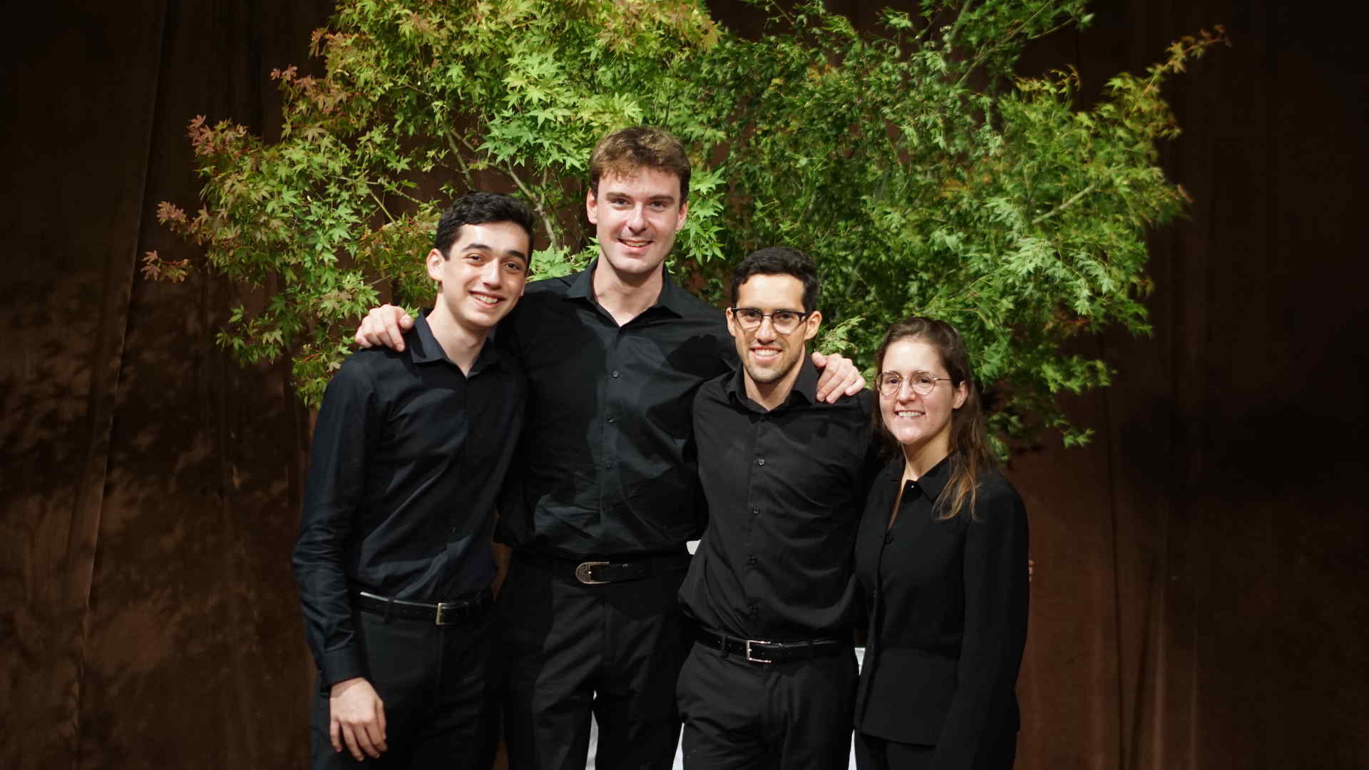 Spencer Rubin and his friends, identified in the photo caption, pose for a group photo in front of a shrub. They are dressed in performance black.