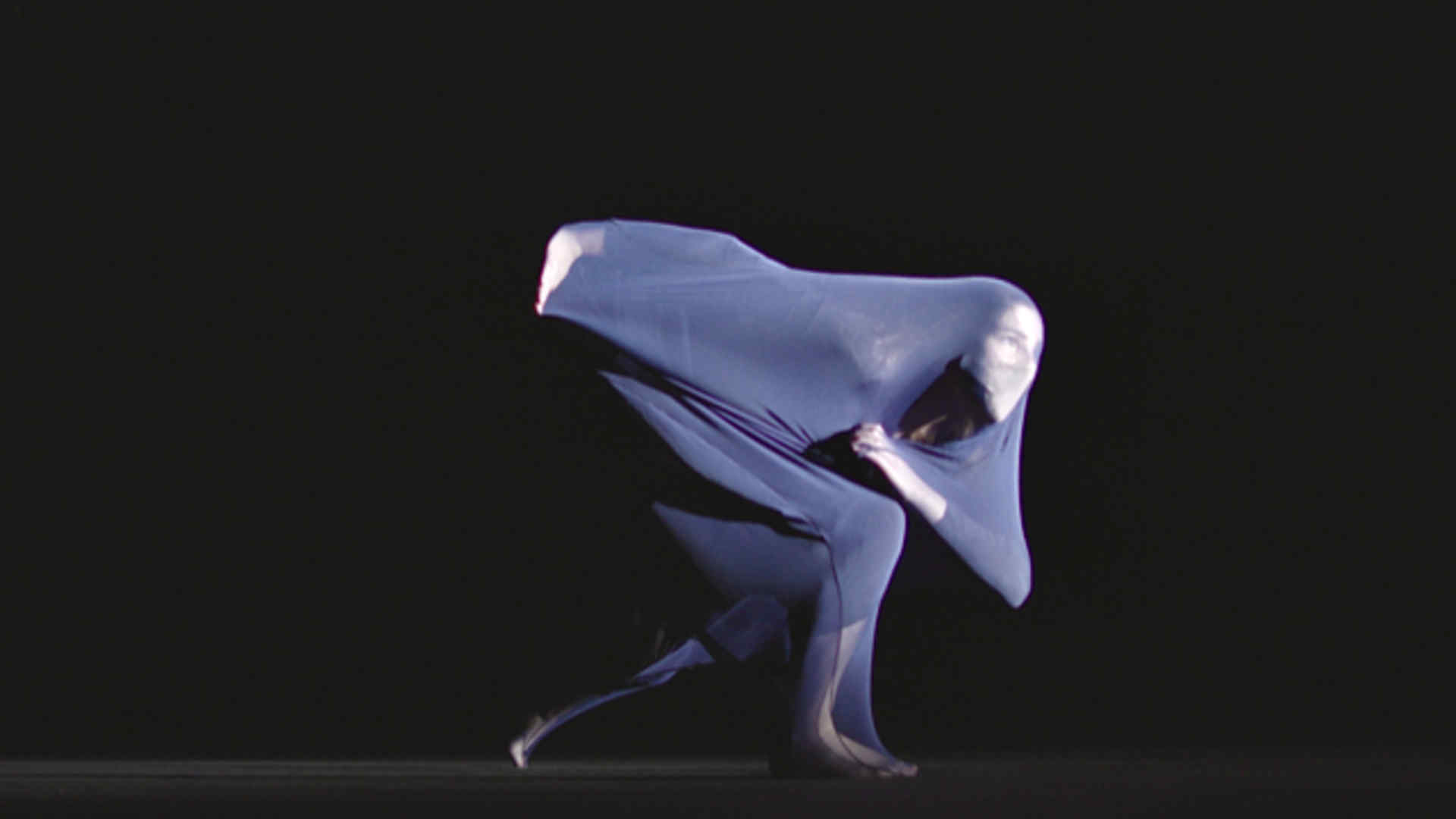 A dancer, costumed in a body sock, poses against a black background