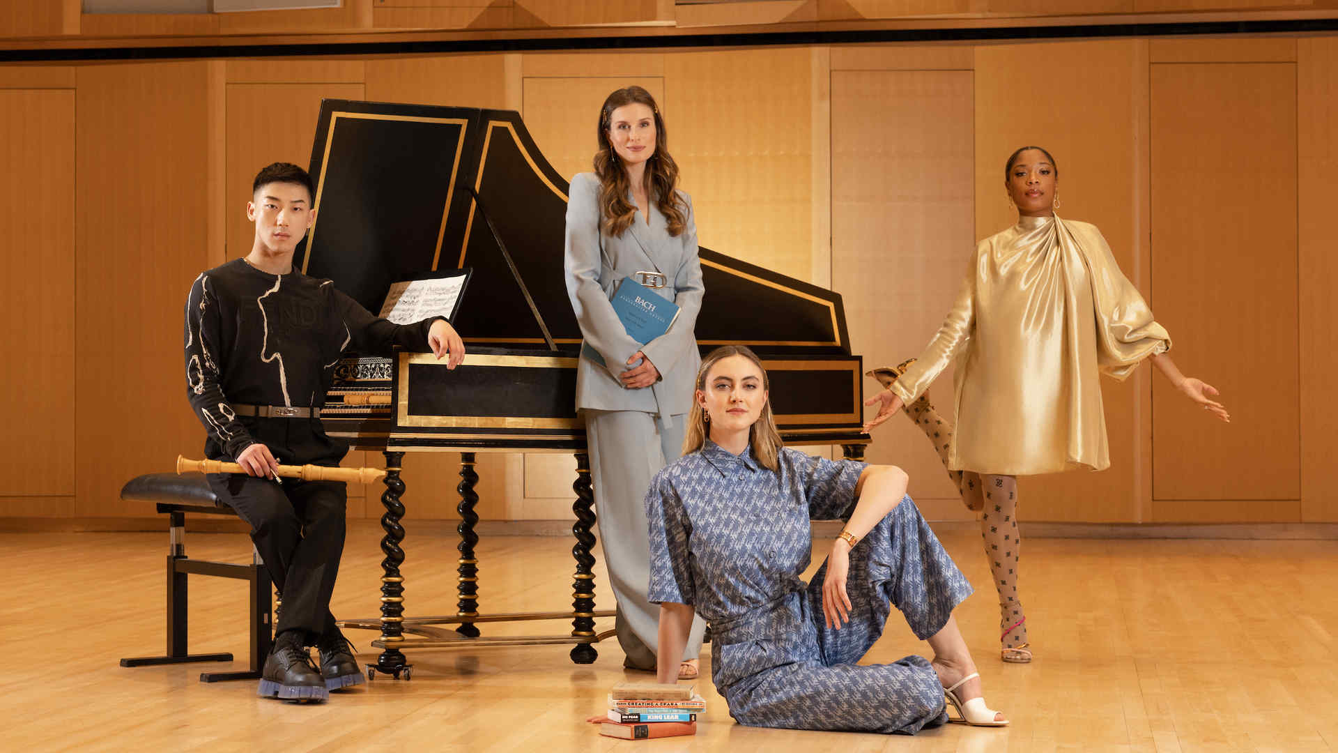 Peter Lim, Mary Beth Nelson, Stella Everett, and Raven Joseph are dressed in high fashion Fendi and pose with books and a harpsichord on stage in a glamor-style shot