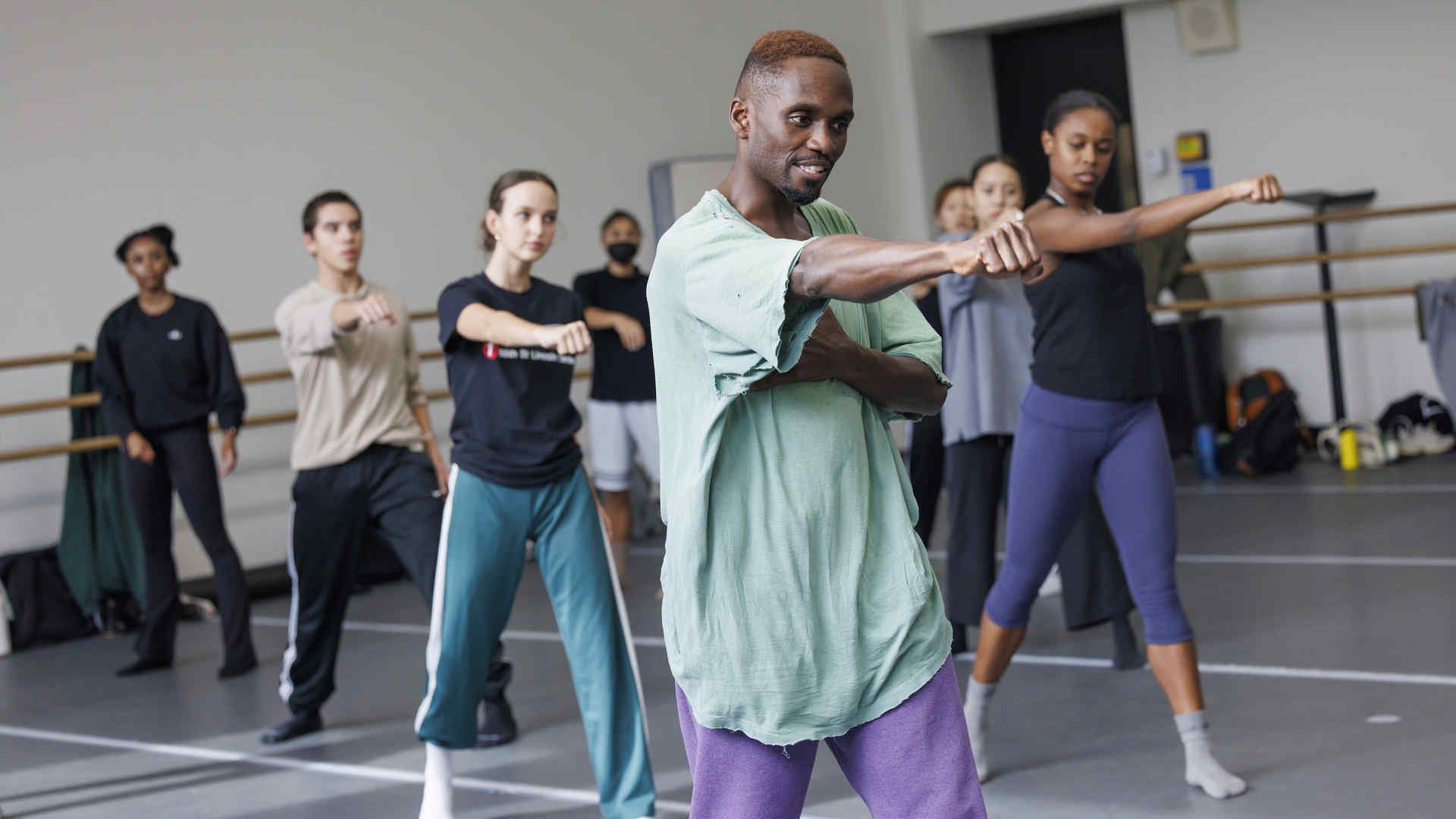 Jermaine Spivey leads a group of dancers through choreography in a dance studio. They make a gesture with the right arm extended.