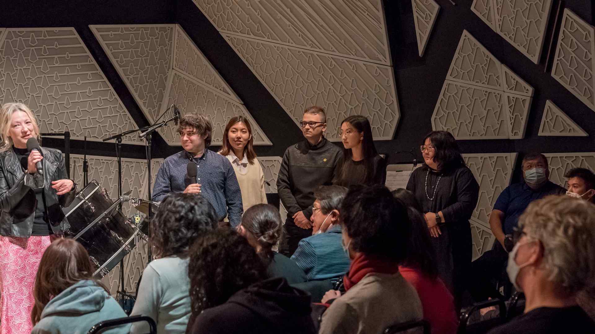 Amy Beth Kirsten, Aidan Gold, SiHyun, Sia Uhm, Eugene Astapov, Lingobo Ma, Nicole Balsirow at the December Blueprint concert. They are all standing on stage and Amy Beth Kirsten, at far left, is speaking into a microphone.