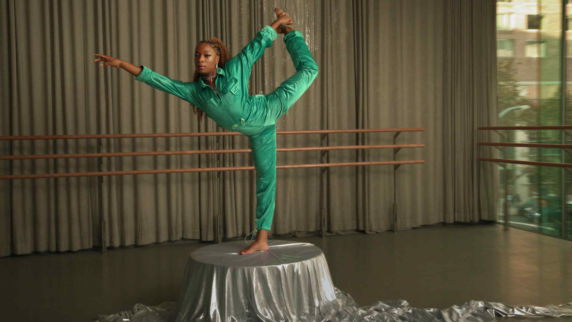 Raven Joseph dressed in a fashionable emerald green jumpsuit posing in a dance studio