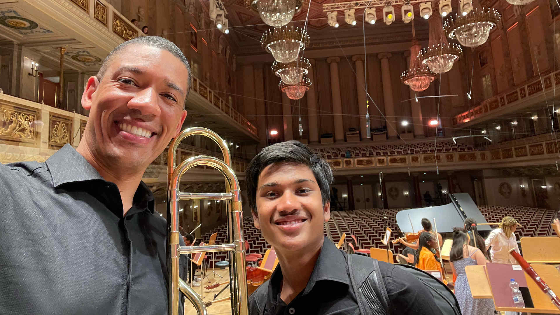 Sprott and Batchu pose for a selfie in a concert hall. They are holding their instruments and smiling.
