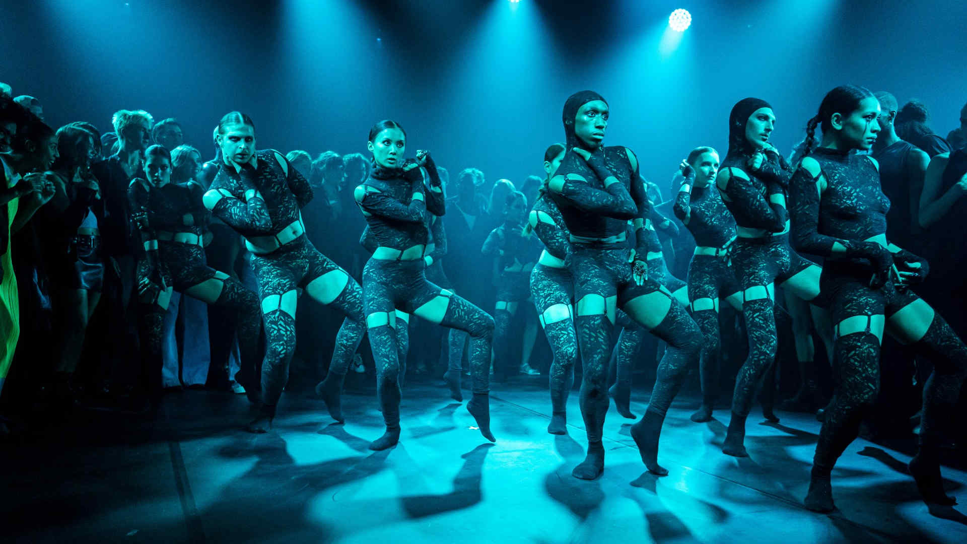 Dancers in lace costumes perform under blue lighting in an immersive dance-rave setting