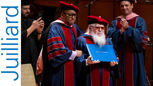 A man with a long beard receiving an honorary degree on a stage